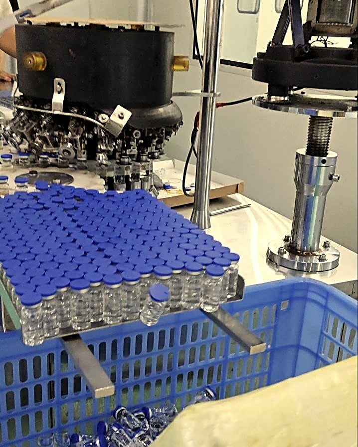 Vial filling and capping line with a tray of blue-capped bottles